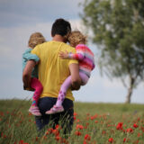 dad holding his two daughters in poppy field