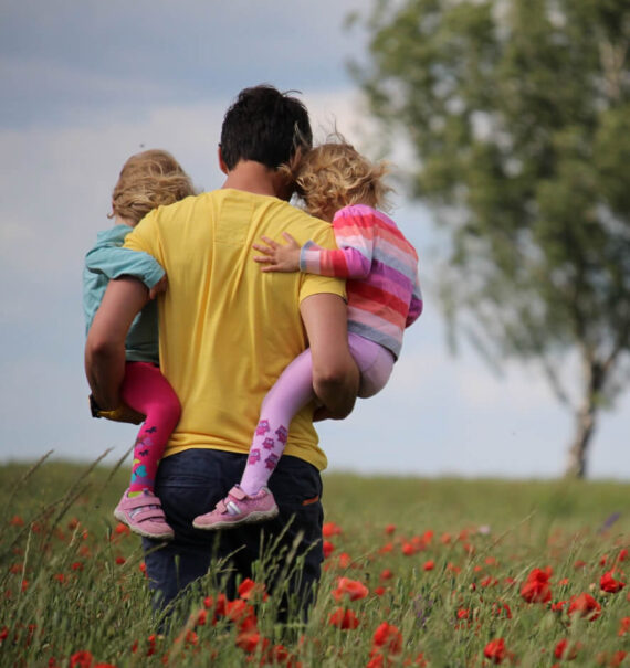 dad holding his two daughters in poppy field